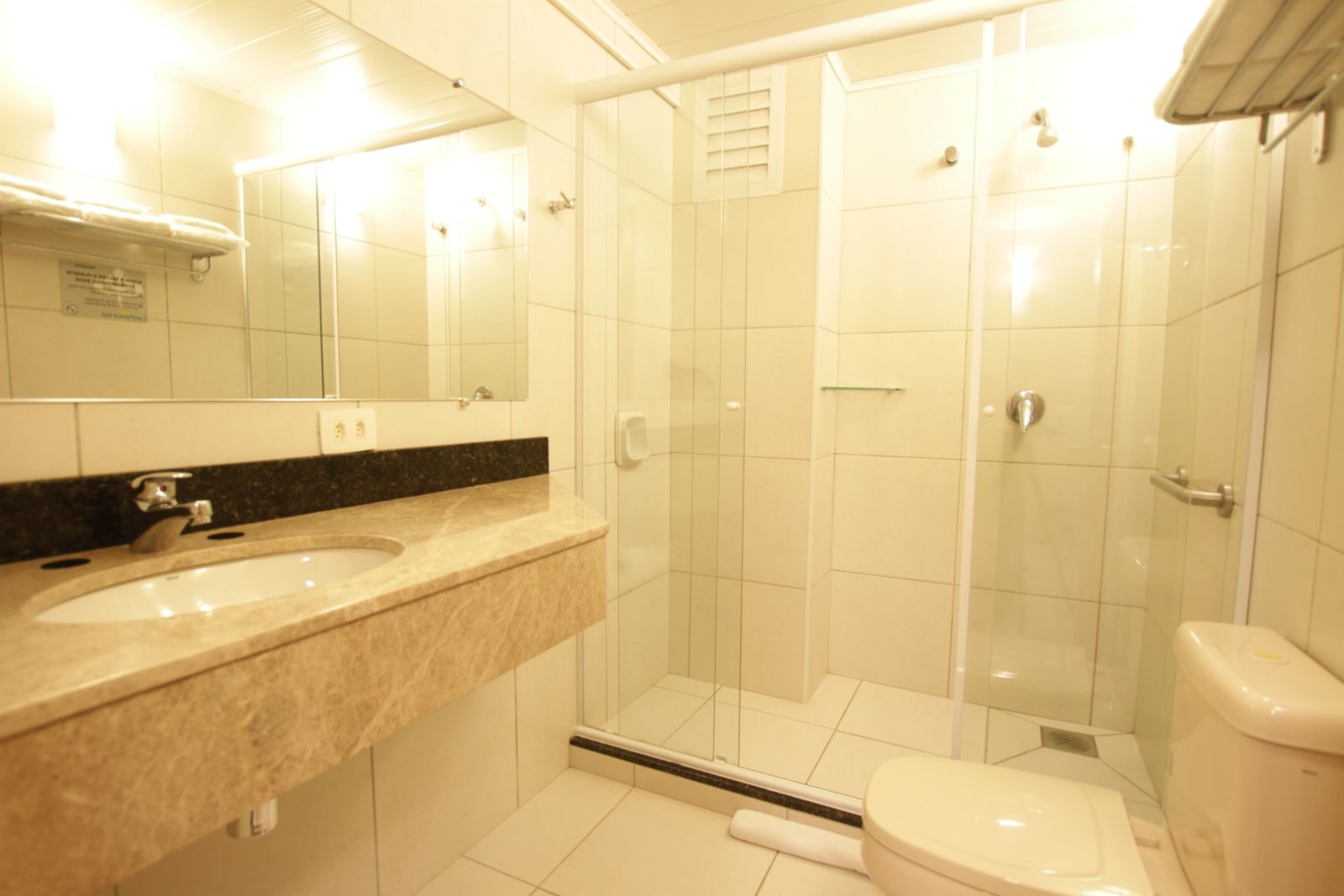 Banheiro do apartamento com box de vidro, bancada em mármore e amenidades — Hotel Confiance Centro Cívico