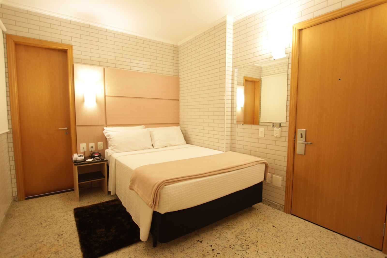 Apartamento Standard Casal com cama de casal, cabeceira em madeira clara e parede de tijolinho branco — Hotel Confiance Centro Cívico